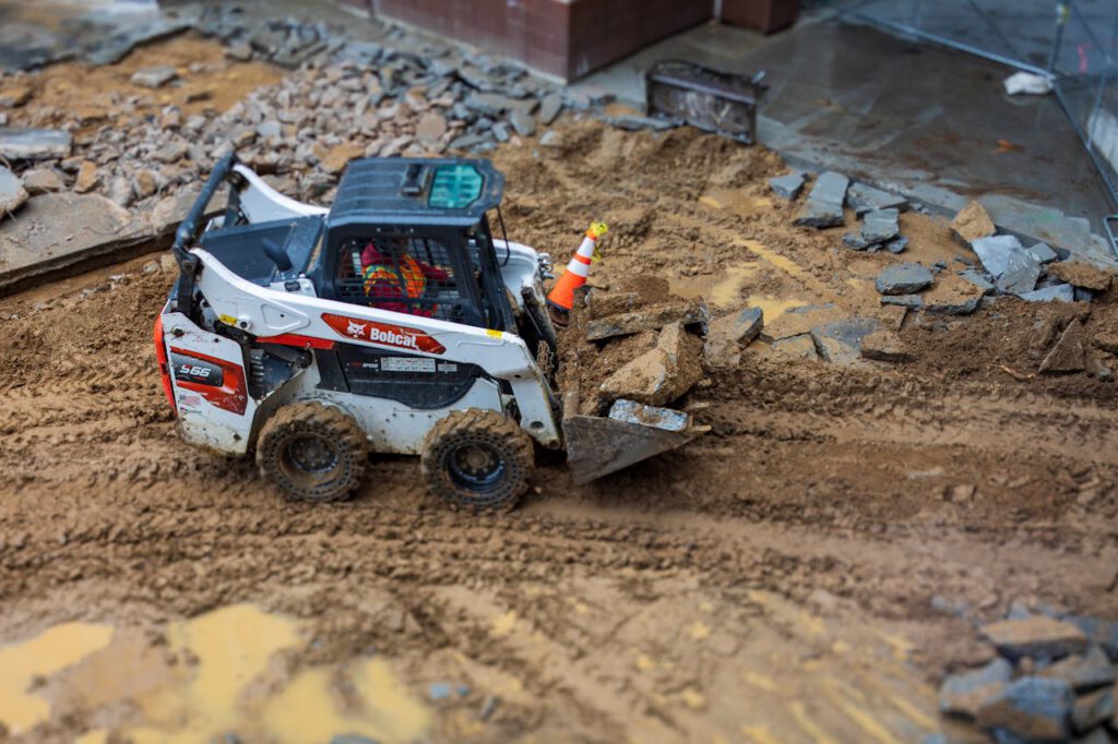 A skid steer loader moves rocks on a muddy construction site, showcasing construction machinery in action.