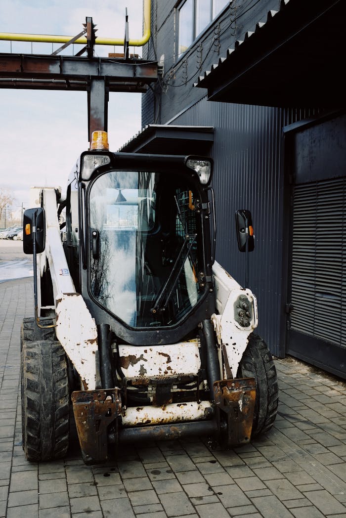 Front view of a rusty bulldozer parked near a black industrial building on a sunny day.
